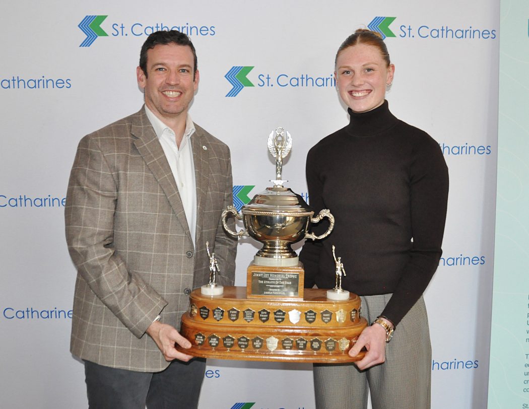 Two people stand together holding an award.