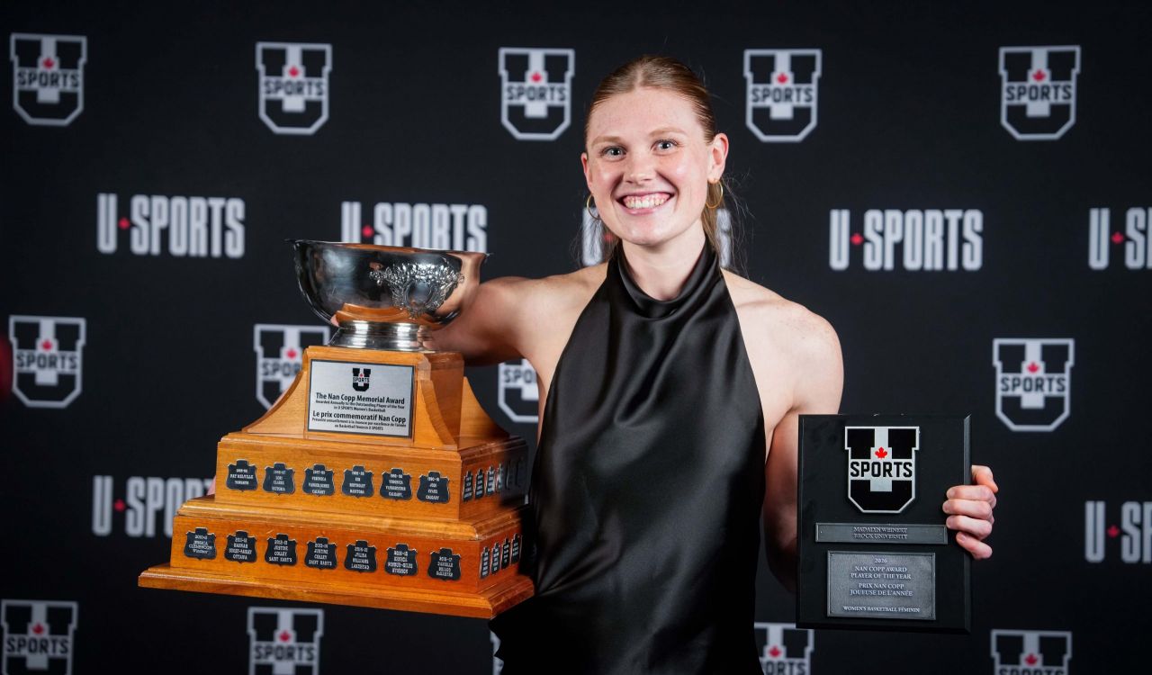 A young woman poses with a trophy and another award.