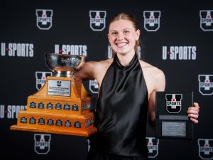 A young woman poses with a trophy and another award.