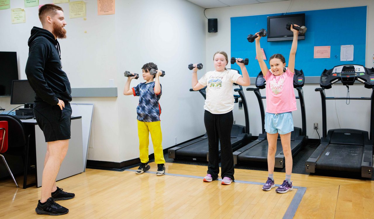 A young man supervises three children who are exercising with small weights.