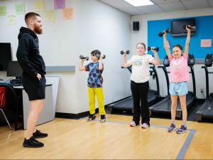 A young man supervises three children who are exercising with small weights.