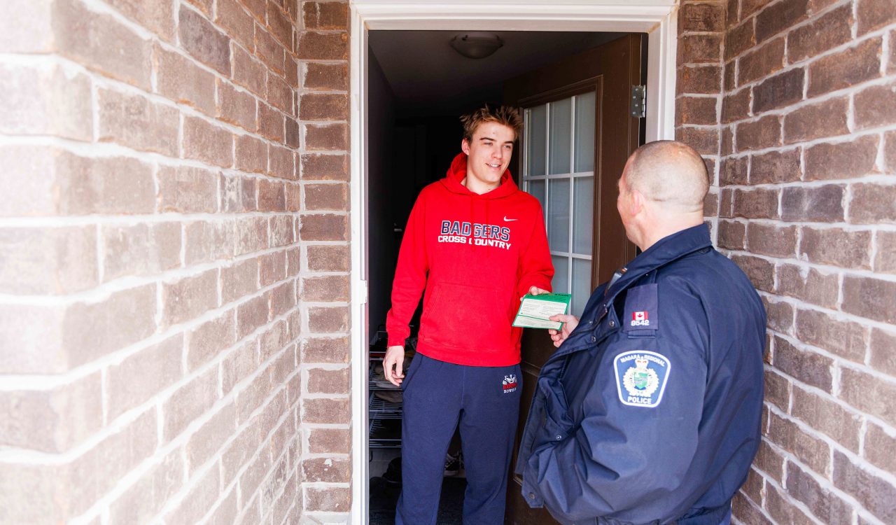 A man takes a paper from another man while standing in the doorway of a home.