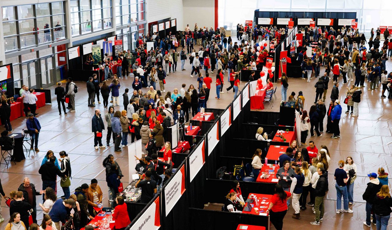 A crowd of people visit various booths set up throughout a gymnasium.