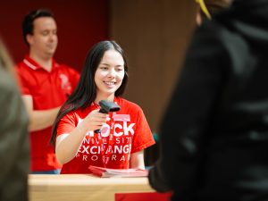 A woman in a red Brock University shirt uses a scanner to check in guests at an event.