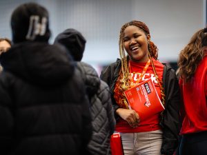 A woman smiles at guests at a university open house event.