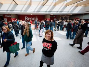 A large group of people mingle and walk around a sunny atrium at a university information fair.