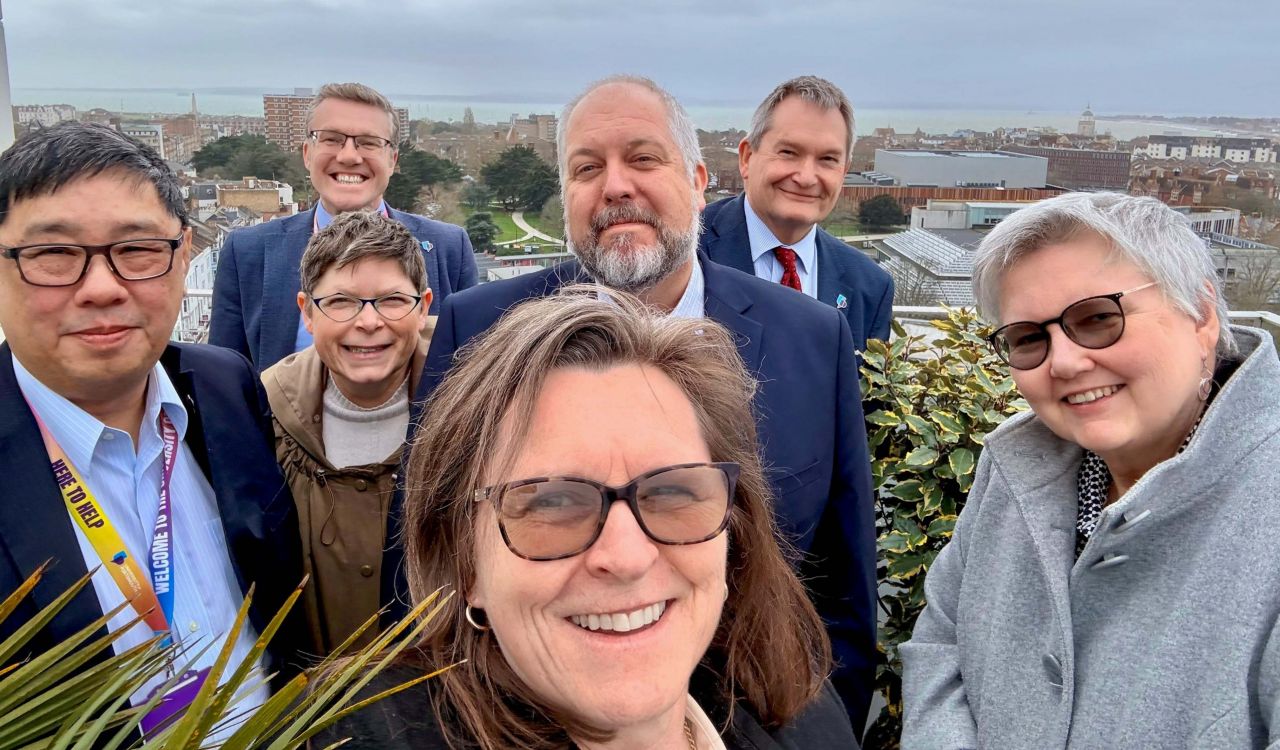 A group of people pose for a selfie with a city and cloudy sky behind them.