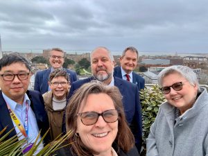 A group of people pose for a selfie with a city and cloudy sky behind them.