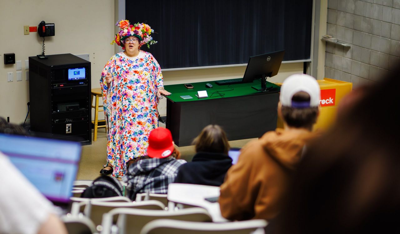 Robyn Bourgeois wearing a crown of flowers and colourful flowered dress at the front of the classroom in October 2025.