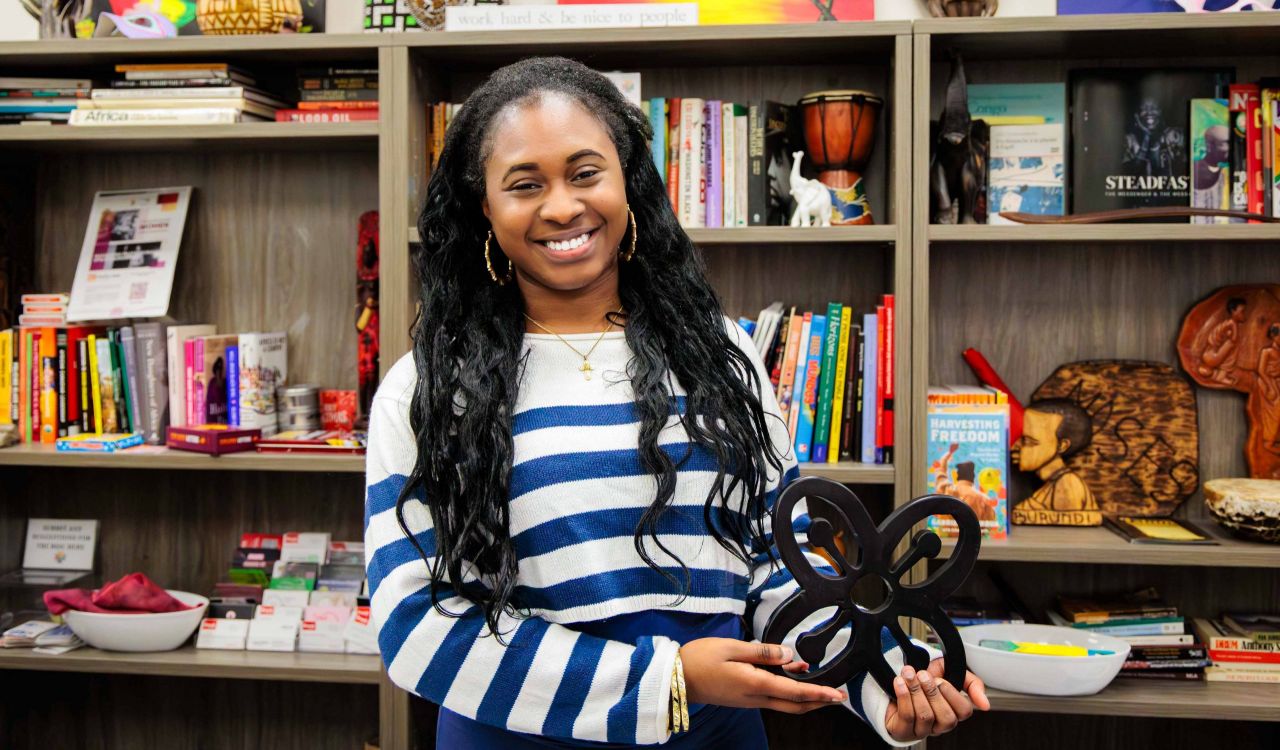 Woman holds a Bese Saka sculpture in front of a wall of books and statues.