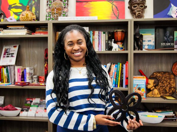 Woman holds a Bese Saka sculpture in front of a wall of books and statues.