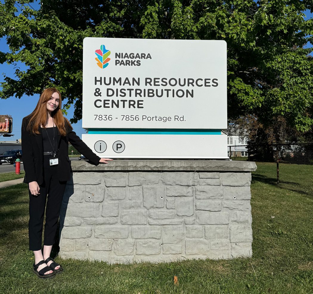 A young woman stands outside beside a Niagara Parks Commission sign.