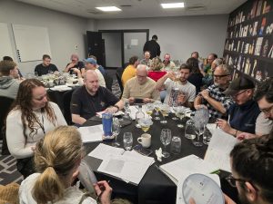 A group of people sit at tables tasting cider and discussing.