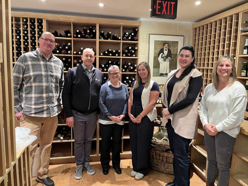 A group of six people pose for a photo in a wine cellar.