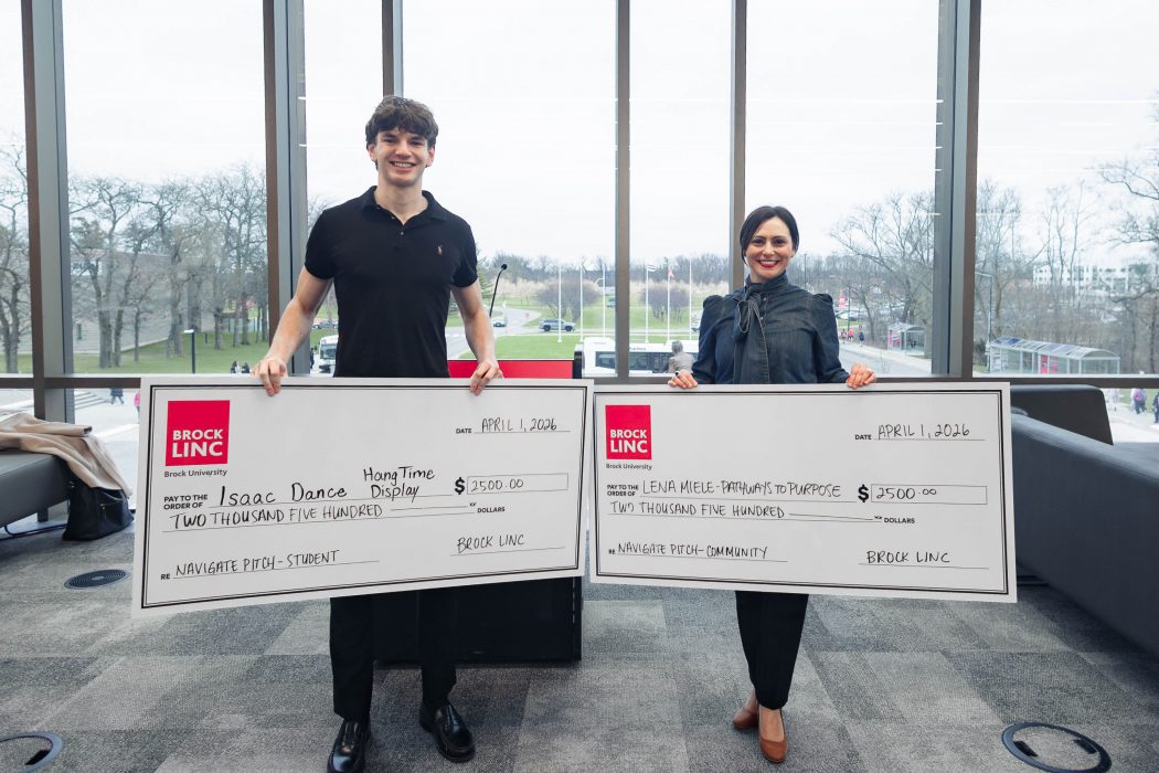 Two people hold giant cheques in a sunny room.