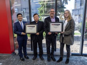The photo has two people in the center who are both receiving plaques from students standing on the outside. The plaque reads Student-Voted Teaching Award.