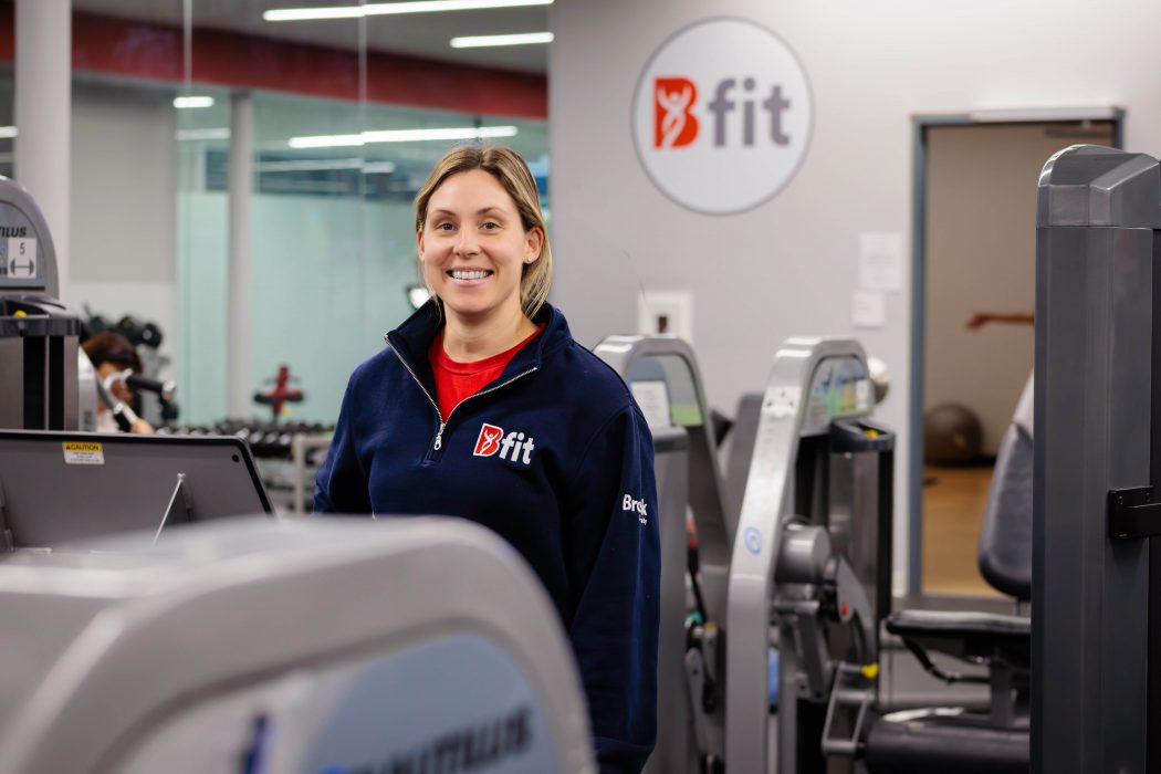 A woman stands beside workout equipment in a gym.