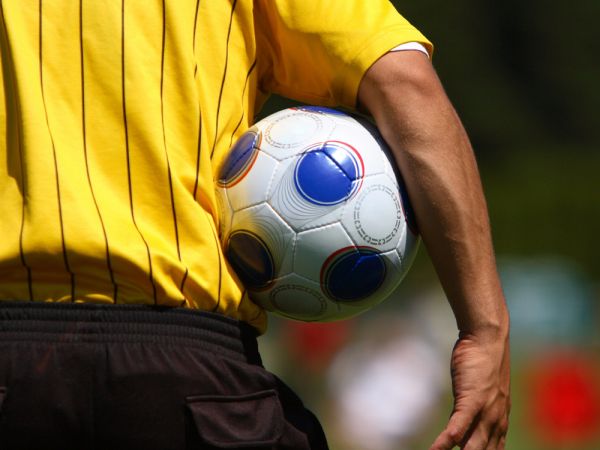 Person in yellow shirt holds a soccer ball and faces playing field.