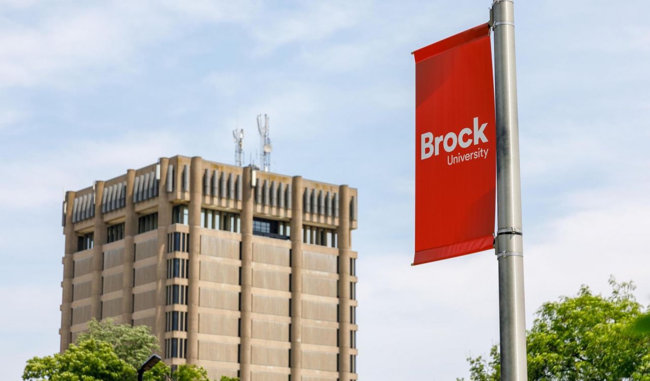 A red Brock University banner hangs from a pole with the Schmon Tower in the background.