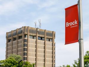 A red Brock University banner hangs from a pole with the Schmon Tower in the background.