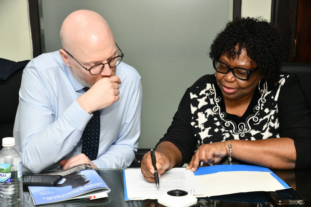 Two people review a document at a table in a boardroom.
