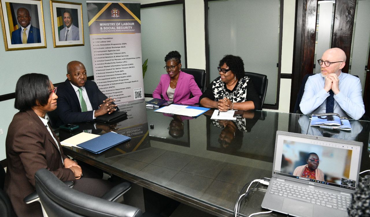 Five people have a meeting around a table in a boardroom.