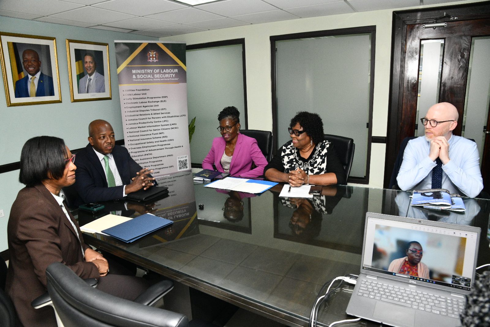 Five people have a meeting around a table in a boardroom.