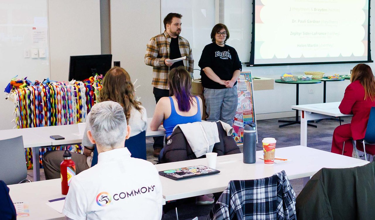 Two people stand side-by-side in a room of people.