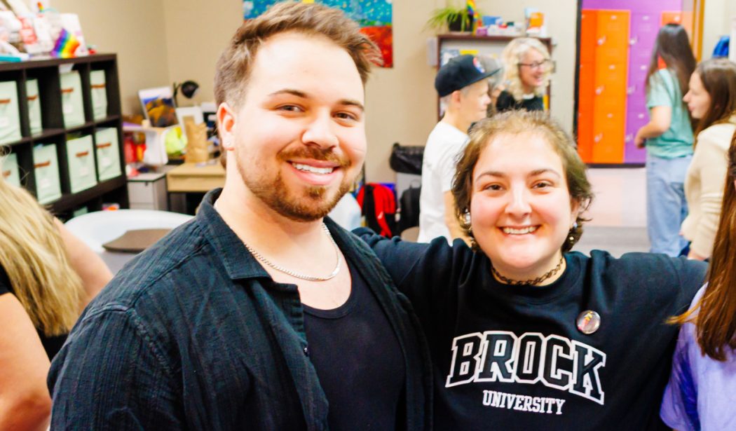 Two people pose for a photo in a busy room.