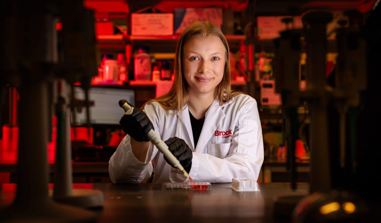 With arms crossed, PhD student Emily Copeland stands next to a machine in a lab.