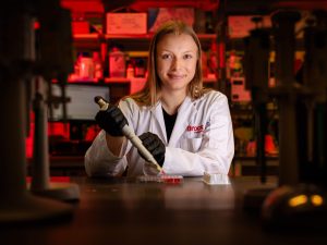 With arms crossed, PhD student Emily Copeland stands next to a machine in a lab.