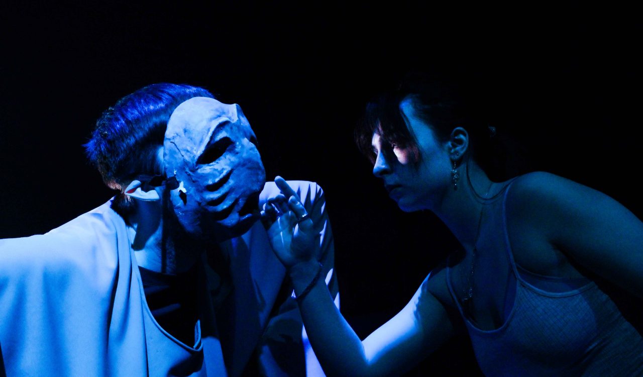 Two people perform on a stage under dark, blue light.