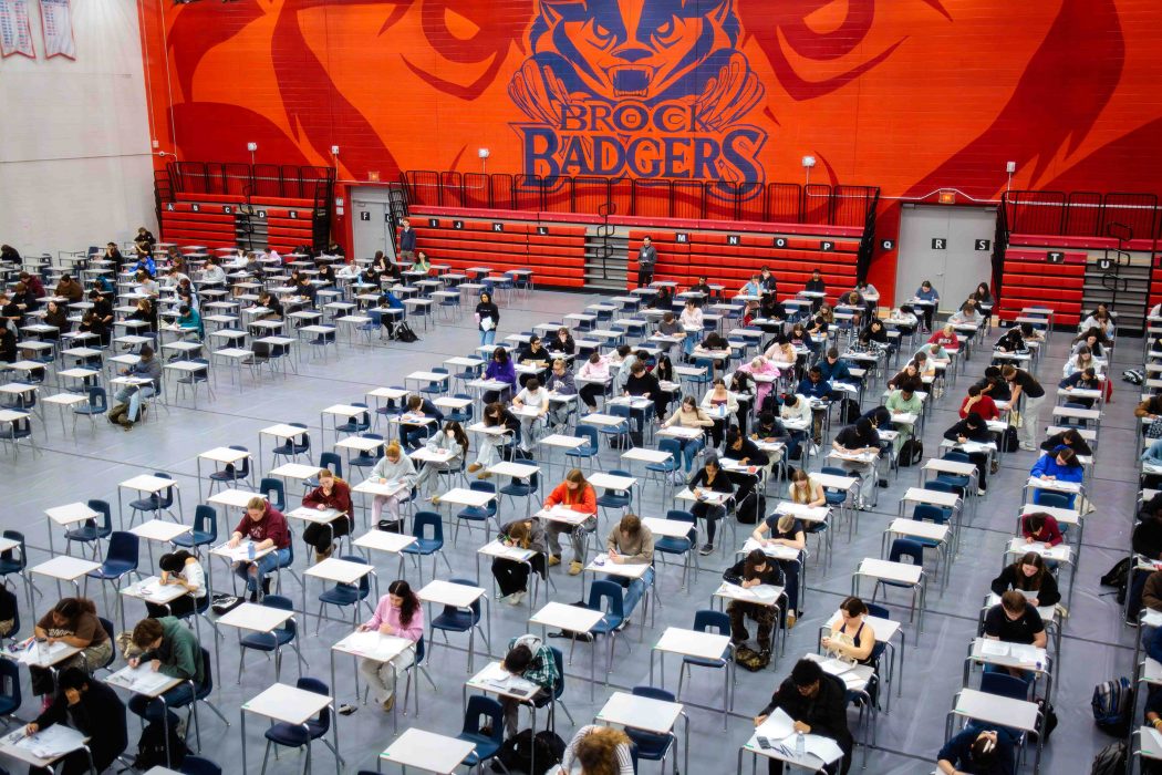 Brock University students sit at rows of desks in a gymnasium writing their exams.