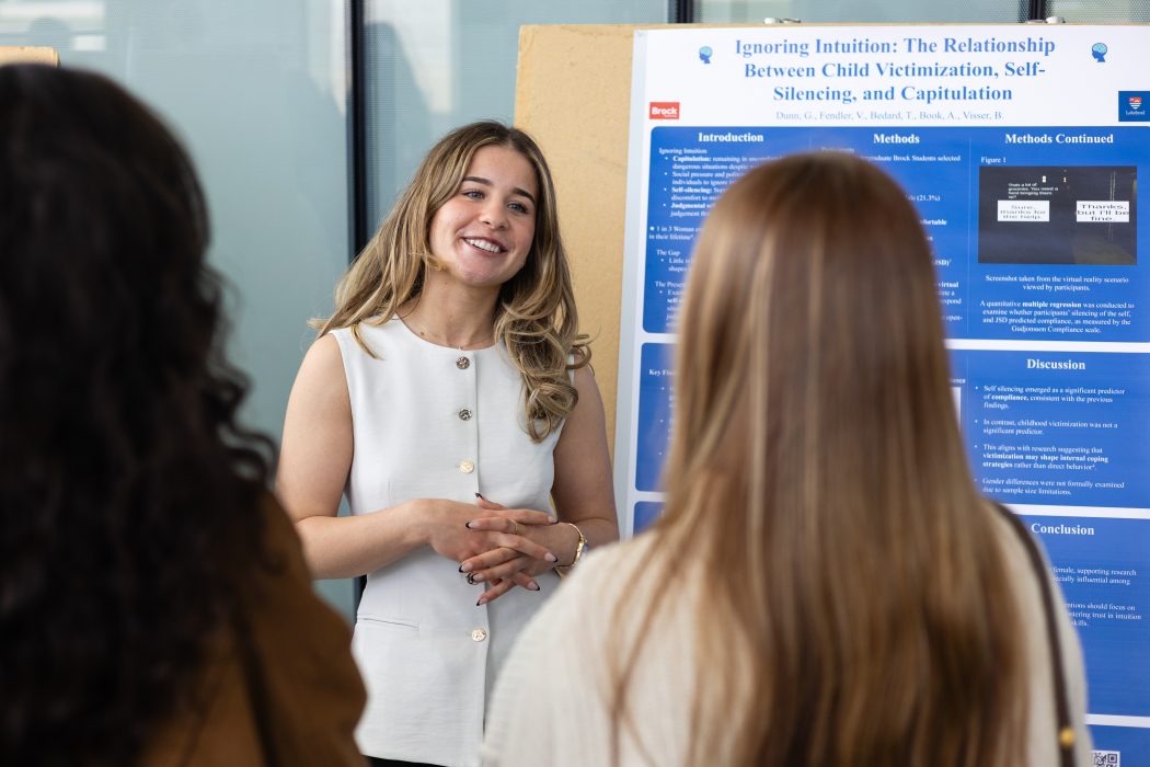 A young woman stands beside a research poster in a sunny university atrium.
