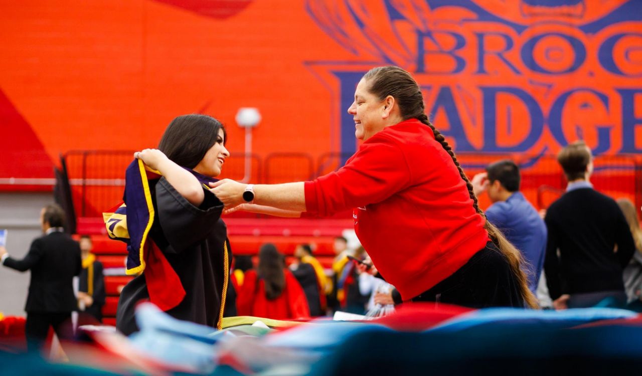 An older woman helps a young woman put on a university graduation