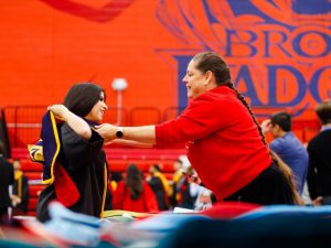 An older woman helps a young woman put on a university graduation