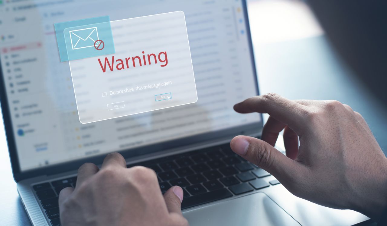 Close-up view of hands typing on a laptop keyboard with email and a warning sign displayed on the screen.