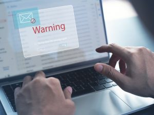 Close-up view of hands typing on a laptop keyboard with email and a warning sign displayed on the screen.