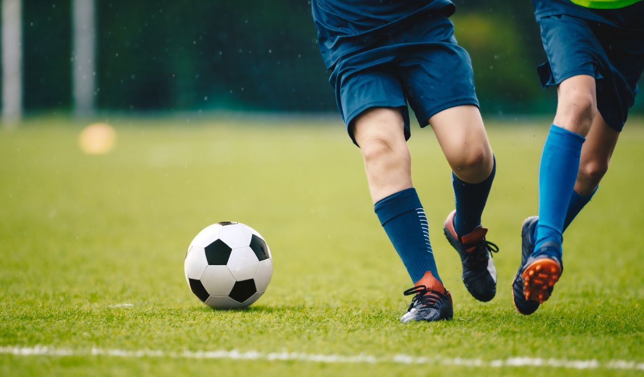 Two soccer players run and chase a ball on a field.
