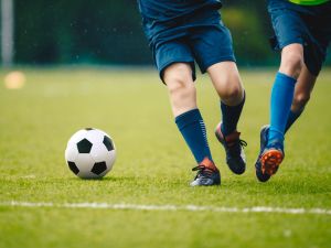 Two soccer players run and chase a ball on a field.