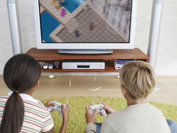Seen from behind, two children play a video game that is visible on the TV in front of them.
