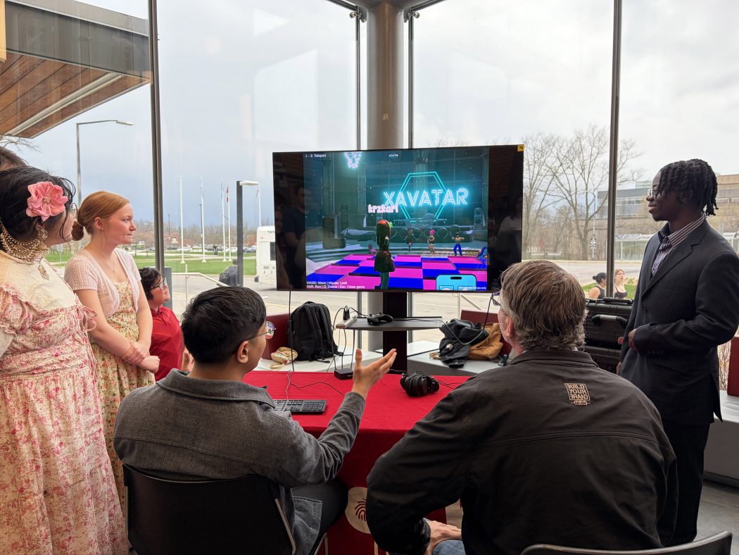 A group of people look on at a TV featuring avatars on a virtual dance space.
