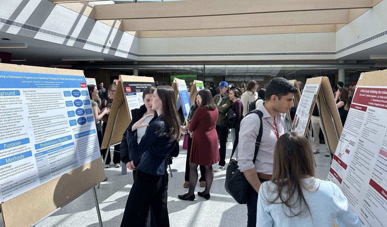 Groups of people looks at research posters in a sunny room.