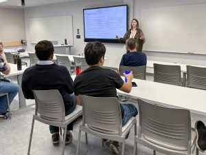 A person speaks to an audience from the front of a university classroom.