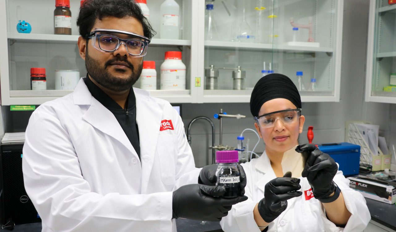 Two people in lab coats pose holding items in a research lab.