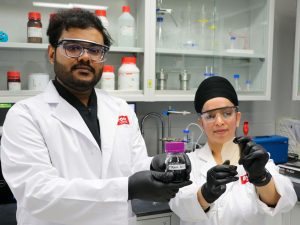 Two people in lab coats pose holding items in a research lab.