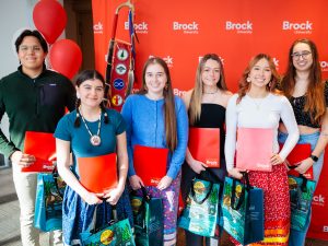 Group of students stand in a row holding red folders.