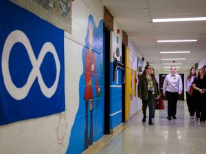 Group of people walk down a hallway in a school.