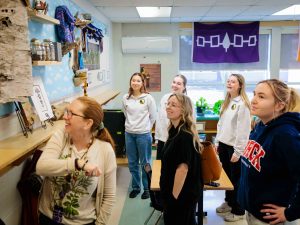 Group of people stand in a circle and talk and point at things hanging on a wall.