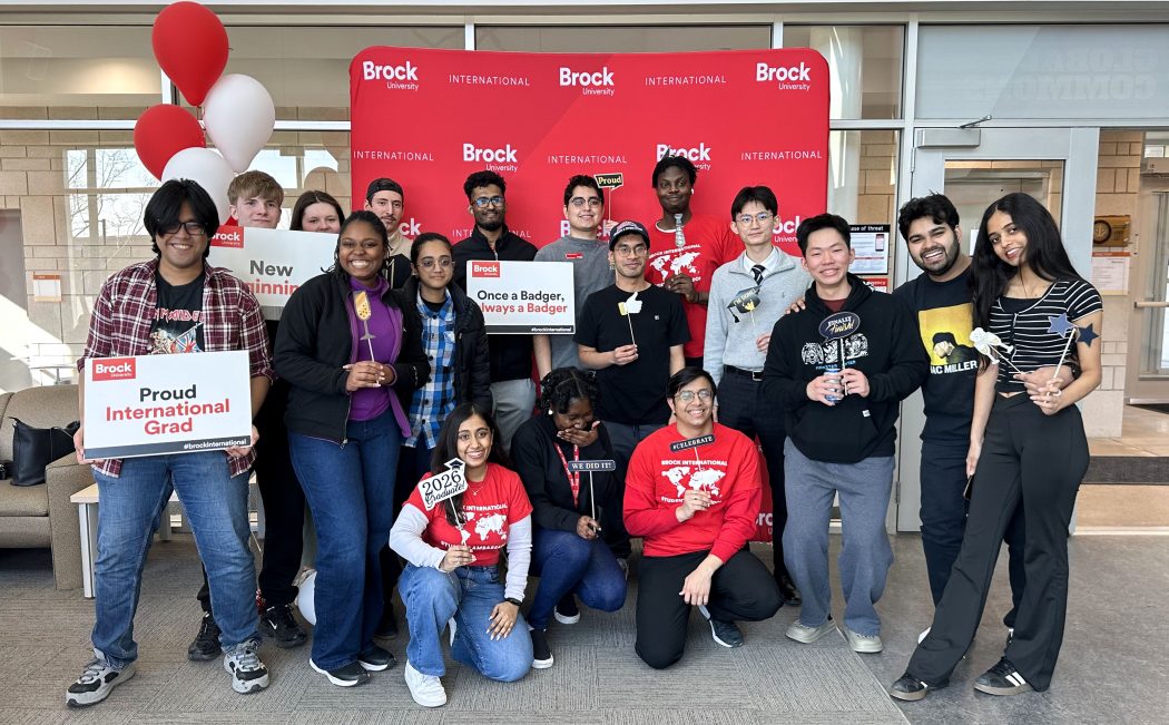 A large group of university students pose for a photo while holding signs.